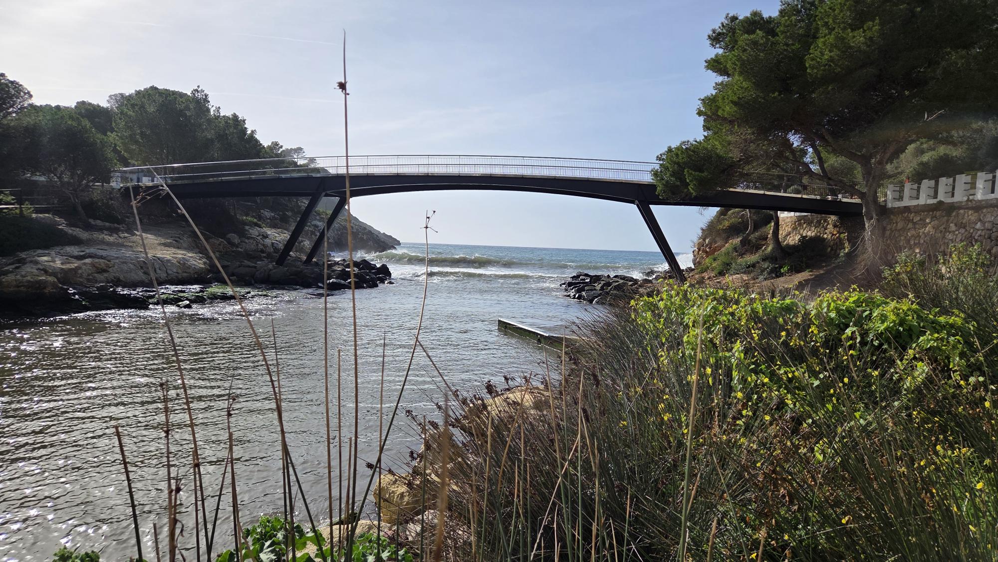 Coastal inlet in Menorca with a small bridge and Mediterranean vegetation leading to the sea